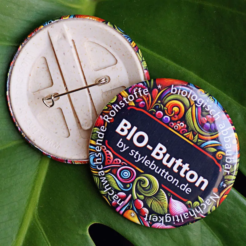 Zwei unserer firmeneigenen Ansteckbuttons, gefertigt aus nachhaltigem Biokunststoff (basierend auf Holz und Stärke), liegen als Symbol für unsere gelebte Nachhaltigkeitskultur auf einem grünen Blatt.